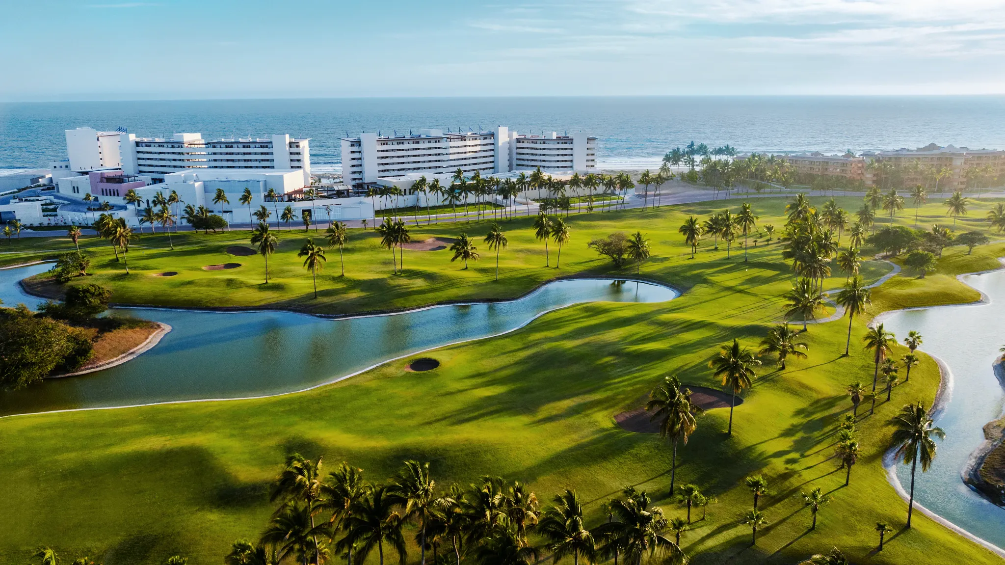 Scenic aerial view of the beachfront golf course at Dreams Estrella del Mar Mazatlan Golf & Spa Resort with palm trees and ocean views.